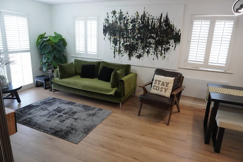 Bright living room with green sofa, wooden floor, area rug, plants and wall art