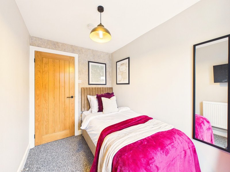Bedroom with single bed, pink bedding, wooden door, pendant light and mirror
