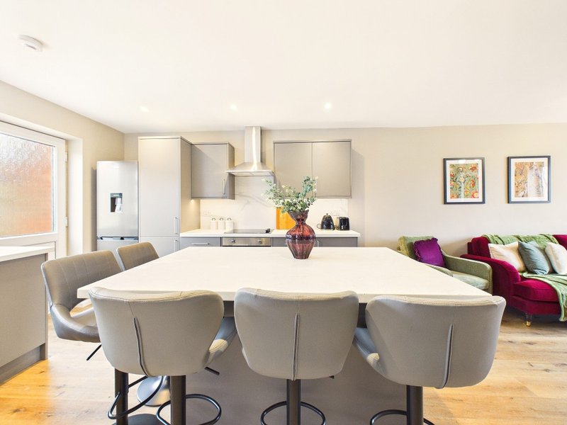Open-plan kitchen and living area with white dining table, grey chairs, and modern appliances