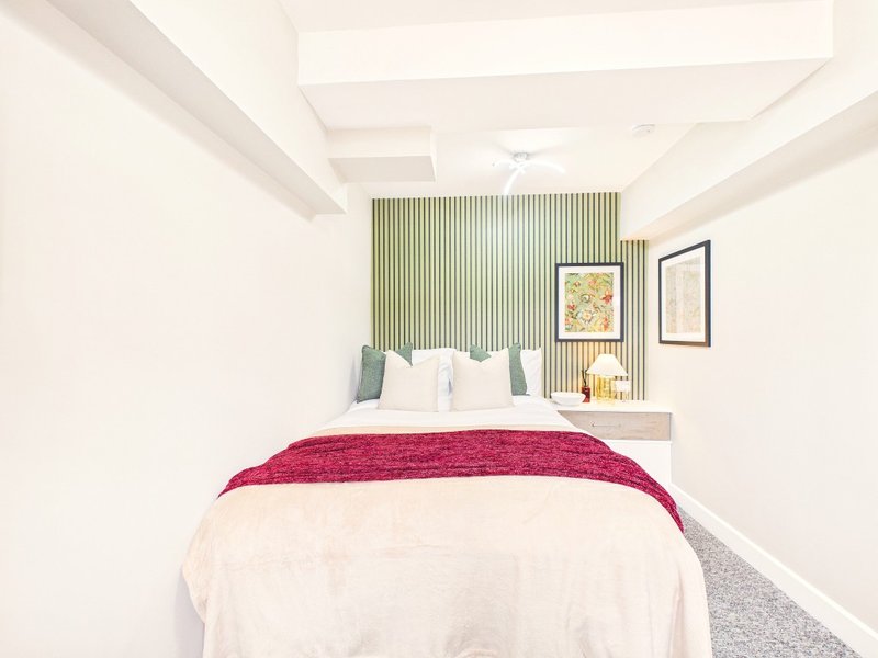 Modern bedroom with double bed, red throw blanket, green striped accent wall and framed artwork