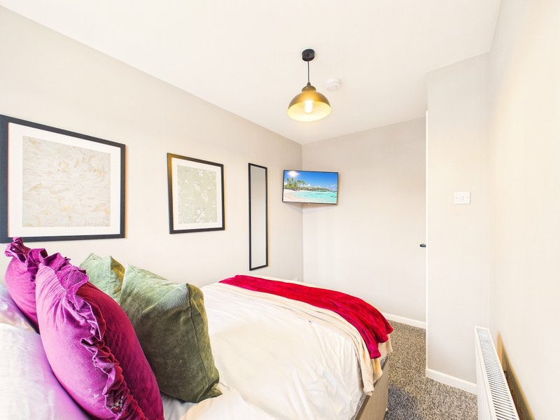 Modern bedroom with double bed, colorful cushions, framed wall art, and pendant lighting
