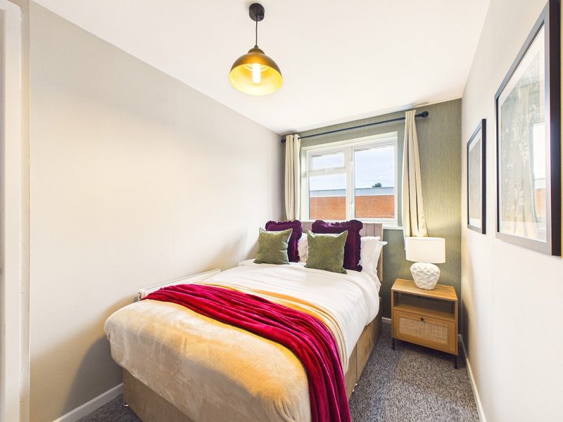 Modern bedroom with double bed, purple and green cushions, red throw, and pendant light
