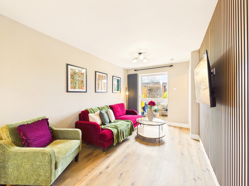 Modern living room with green and magenta upholstered seating, wooden flooring, framed wall art and garden view