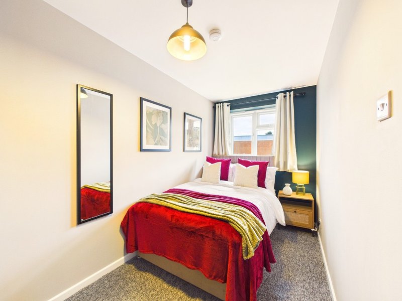 Bright bedroom with double bed, colorful bedding, mirror, framed wall art, and window with curtains