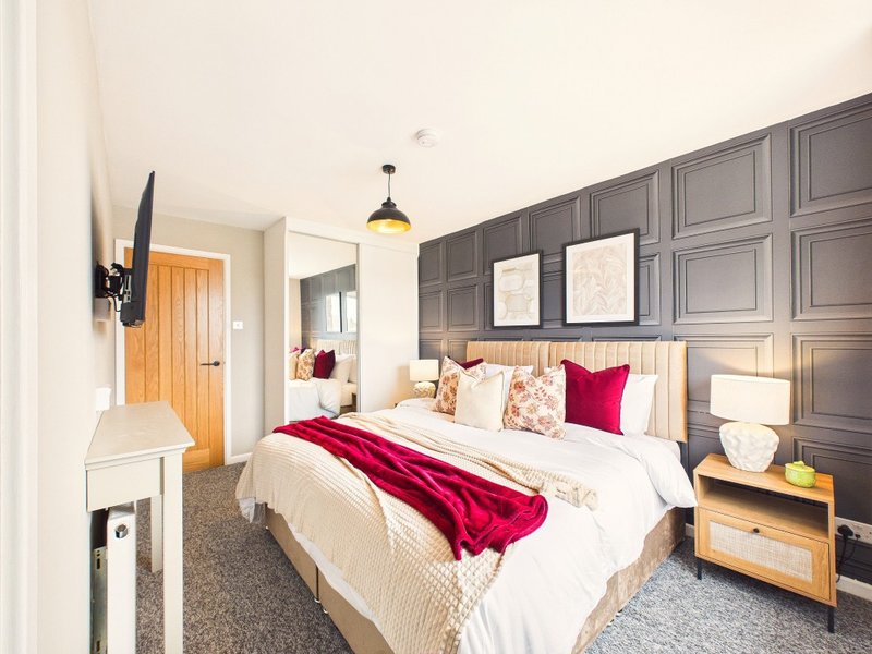 Modern bedroom with double bed, grey paneled wall, red accents, and pendant light