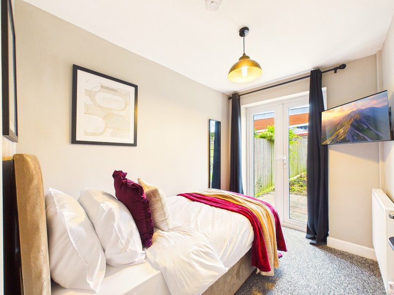 Bright bedroom with double bed, white pillows, burgundy throw, pendant light and glass doors