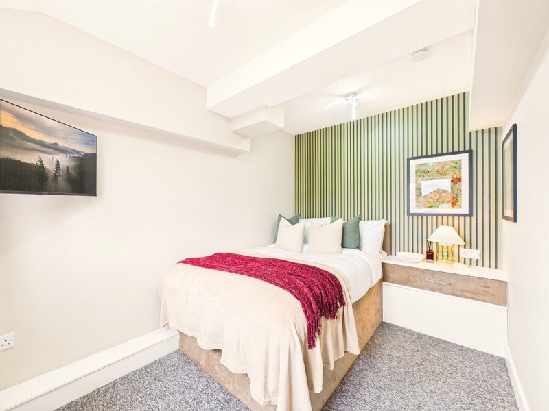 Modern bedroom with double bed, red throw, green accent wall and framed artwork
