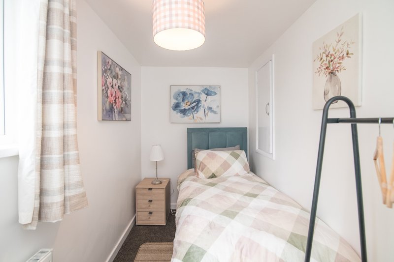 Compact bedroom with single bed, wooden nightstand, framed artwork, and checkered curtains