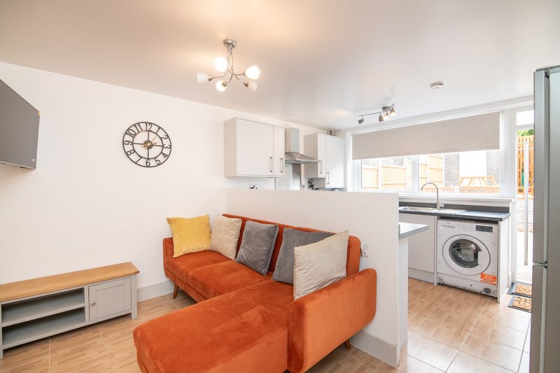 Open-plan living room and kitchen with orange sofa, wall clock, and modern appliances