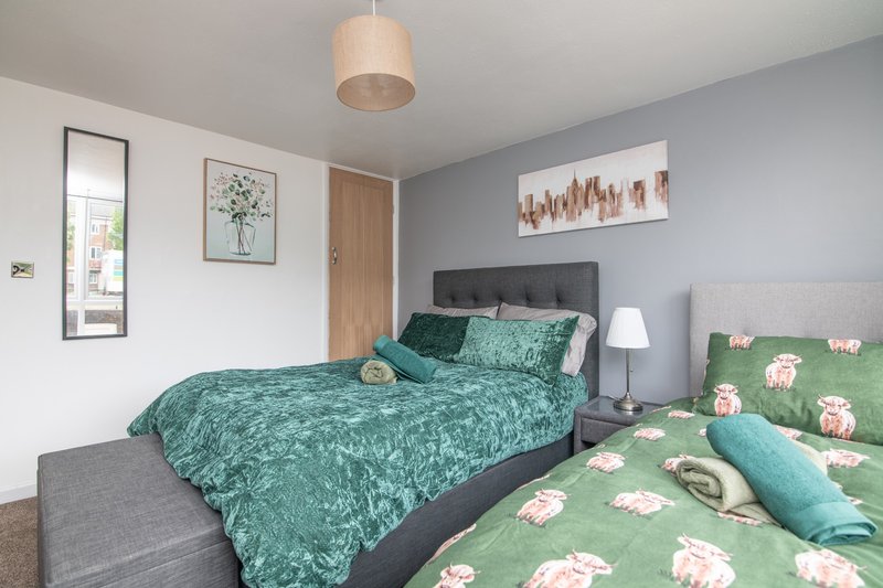 Bright bedroom with two beds, teal bedding, grey headboards, pendant light and wall art