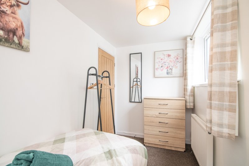 Compact bedroom with single bed, wooden chest of drawers, and window with checkered curtains