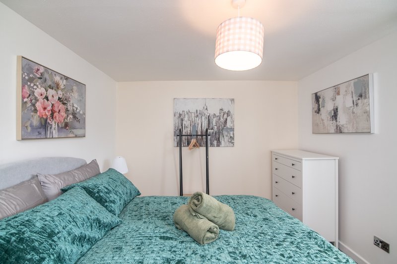 Bright bedroom with teal bedding, framed floral artwork, white dresser and ceiling light