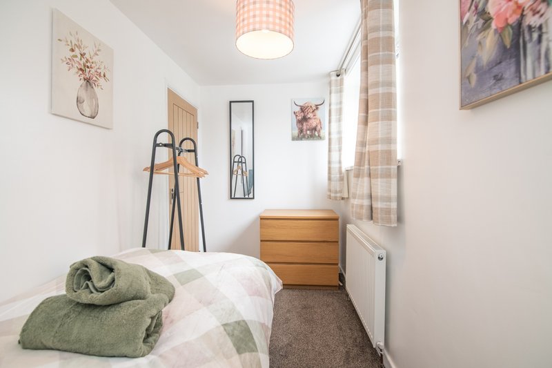 Compact bedroom with single bed, wooden chest of drawers, and window with checkered curtains