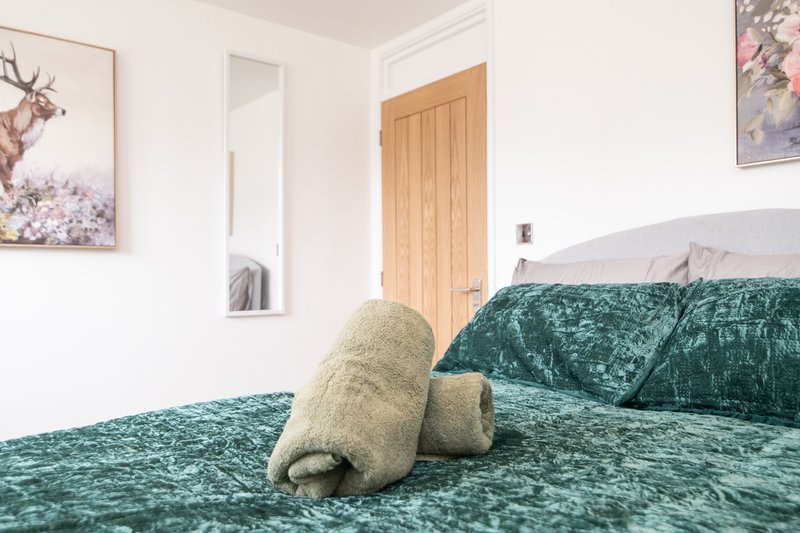 Bedroom with double bed, green velvet bedding, rolled towels, wooden door and wall art