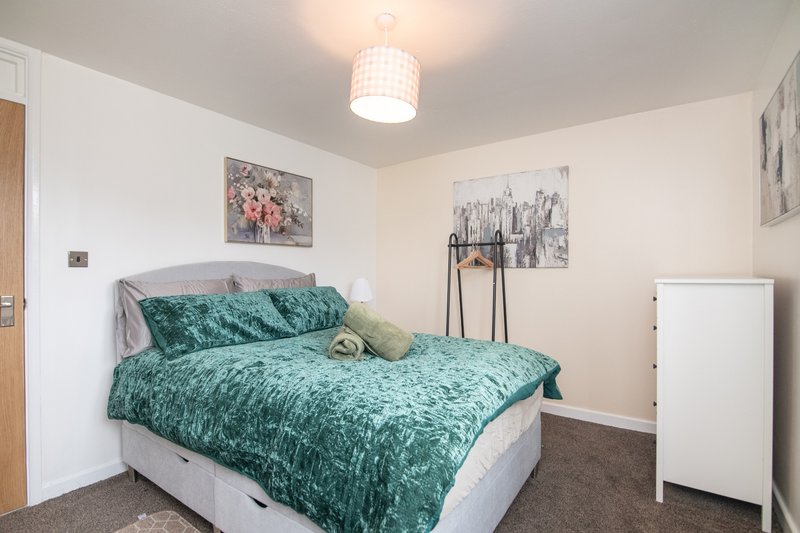 Bedroom with double bed, green bedding, white furniture and framed wall art