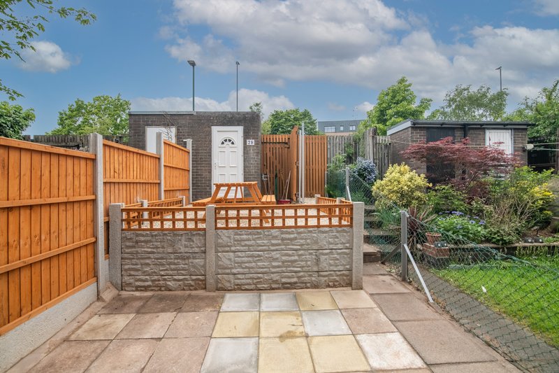 Paved garden patio with wooden fence, seating area and neighbouring properties visible