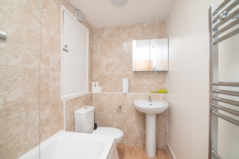Bathroom with beige tile walls, white toilet, pedestal sink, mirror cabinet and towel rail
