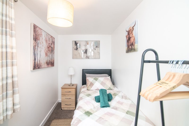 Compact bedroom with single bed, bunk frame, wooden nightstand and wall art