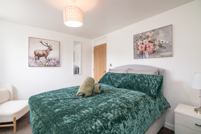 Bedroom with double bed, green velvet bedding, framed artwork, ceiling light fixture and white walls