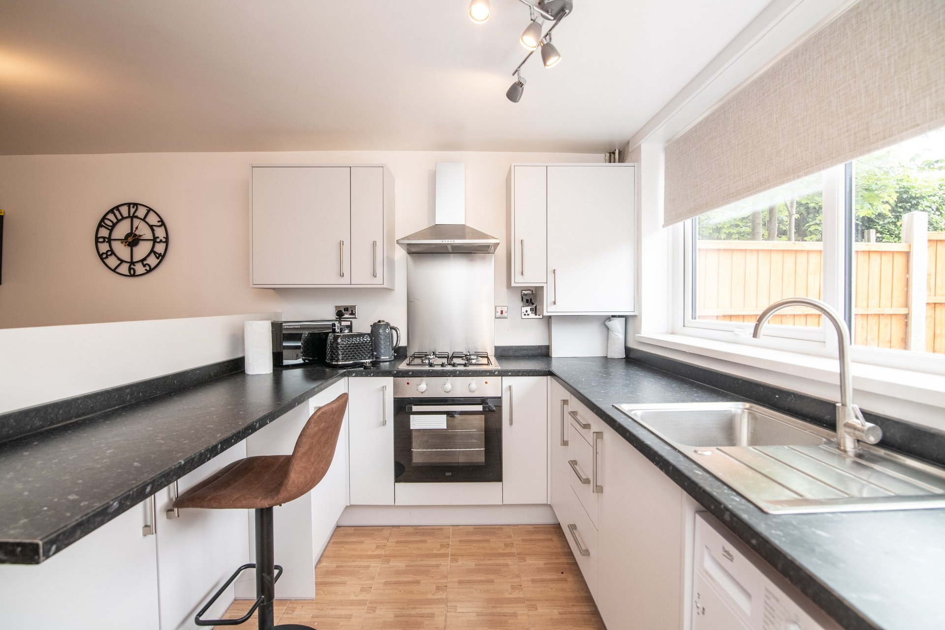 Modern kitchen with white cabinetry, black countertops, stainless steel appliances and wooden flooring