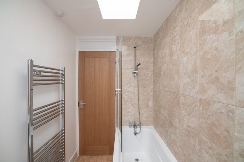 Modern bathroom with bathtub, glass shower screen, heated towel rail and beige tile walls