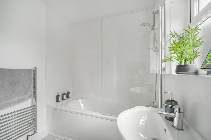 Modern bathroom with white suite, glass shower enclosure, heated towel rail and potted plant