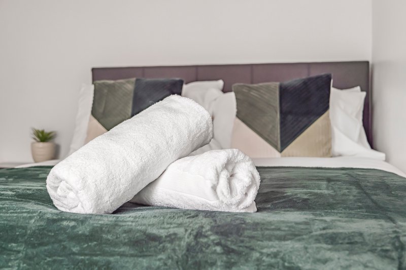 Bedroom with rolled white towels on green bedspread and upholstered headboard