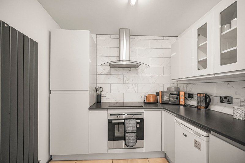 Modern kitchen with white cabinetry, black countertops, stainless steel range hood and appliances