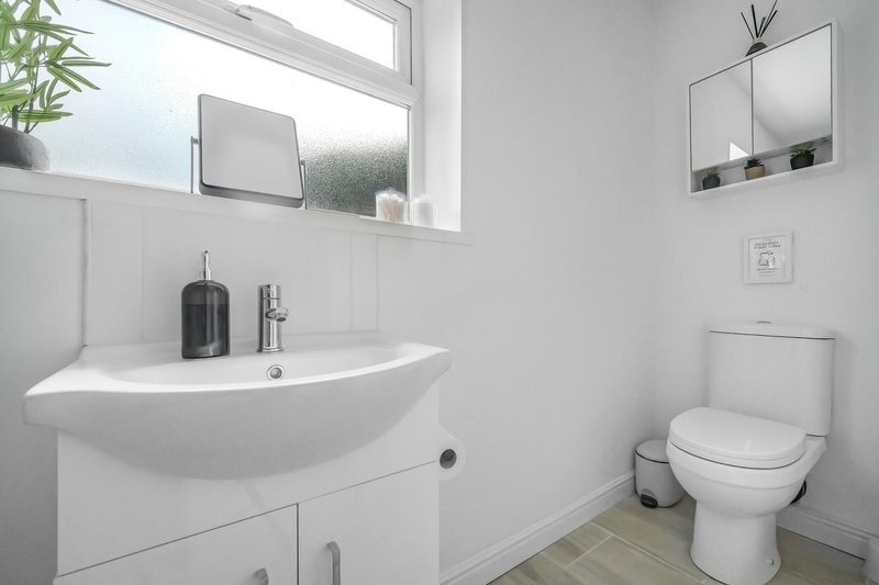Modern bathroom with curved white sink, mirror, toilet, and large window with natural light