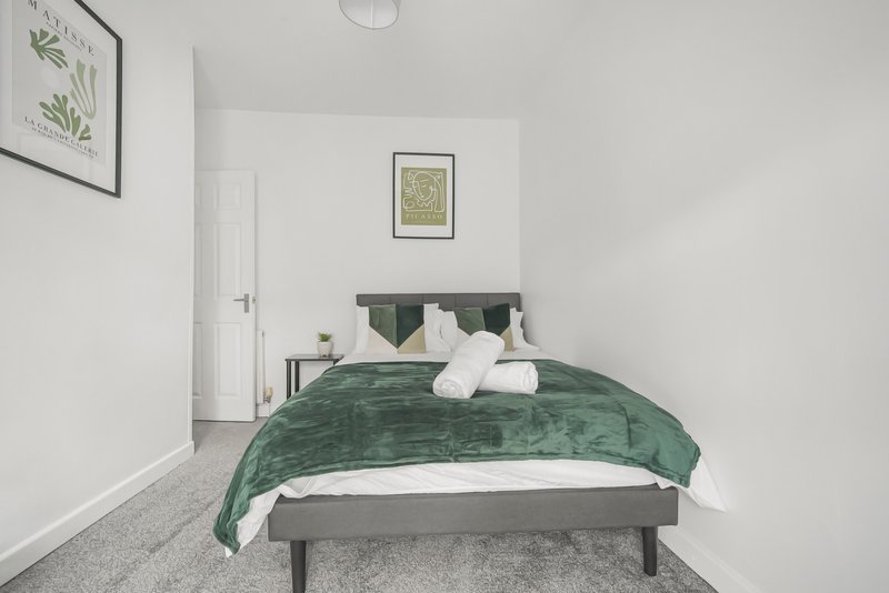 Bedroom with double bed, green velvet bedding, white pillows, framed wall art, and grey carpet flooring