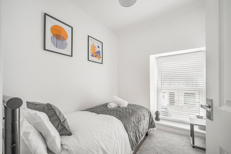 Bright modern bedroom with single bed, white bedding, grey throw, and framed wall art