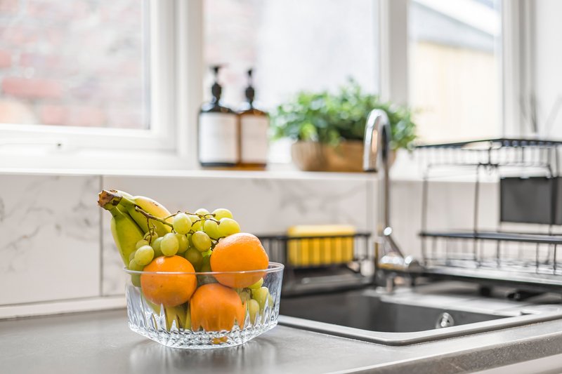 Modern kitchen with marble countertop, fresh fruit bowl, sink and window with plants