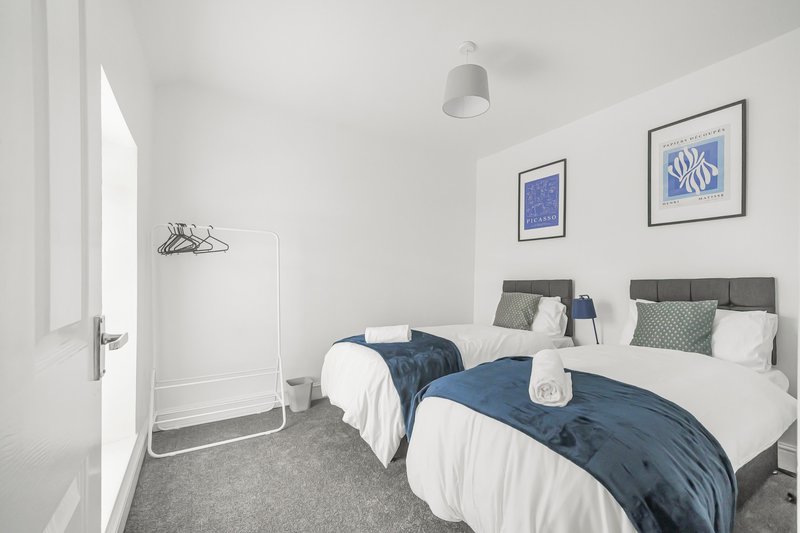Bright bedroom with two single beds, grey headboards, blue bedding, white walls and framed artwork