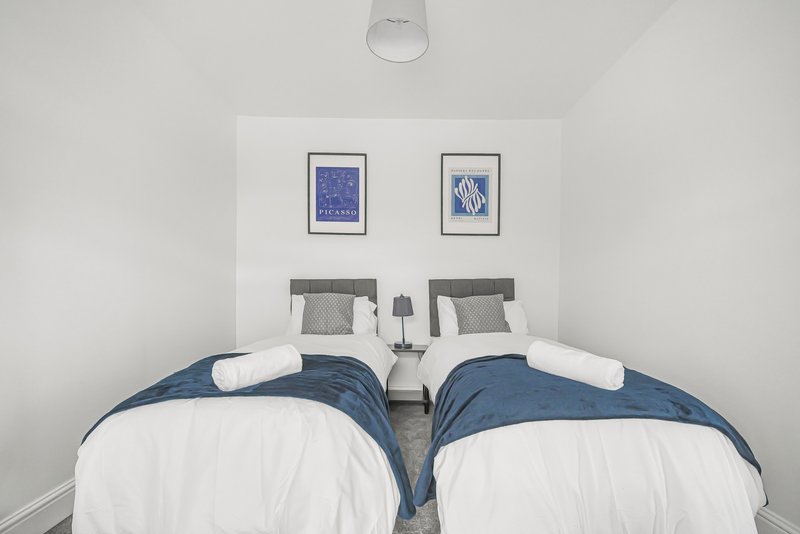 Twin bedroom with two beds, white bedding, blue throws, framed wall art, and pendant light