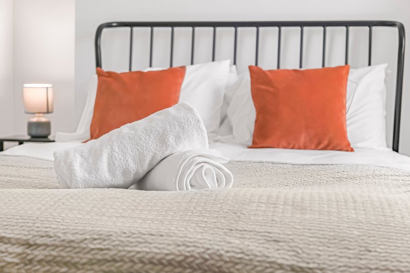 Modern bedroom with metal headboard, white bedding, orange pillows and bedside lamp