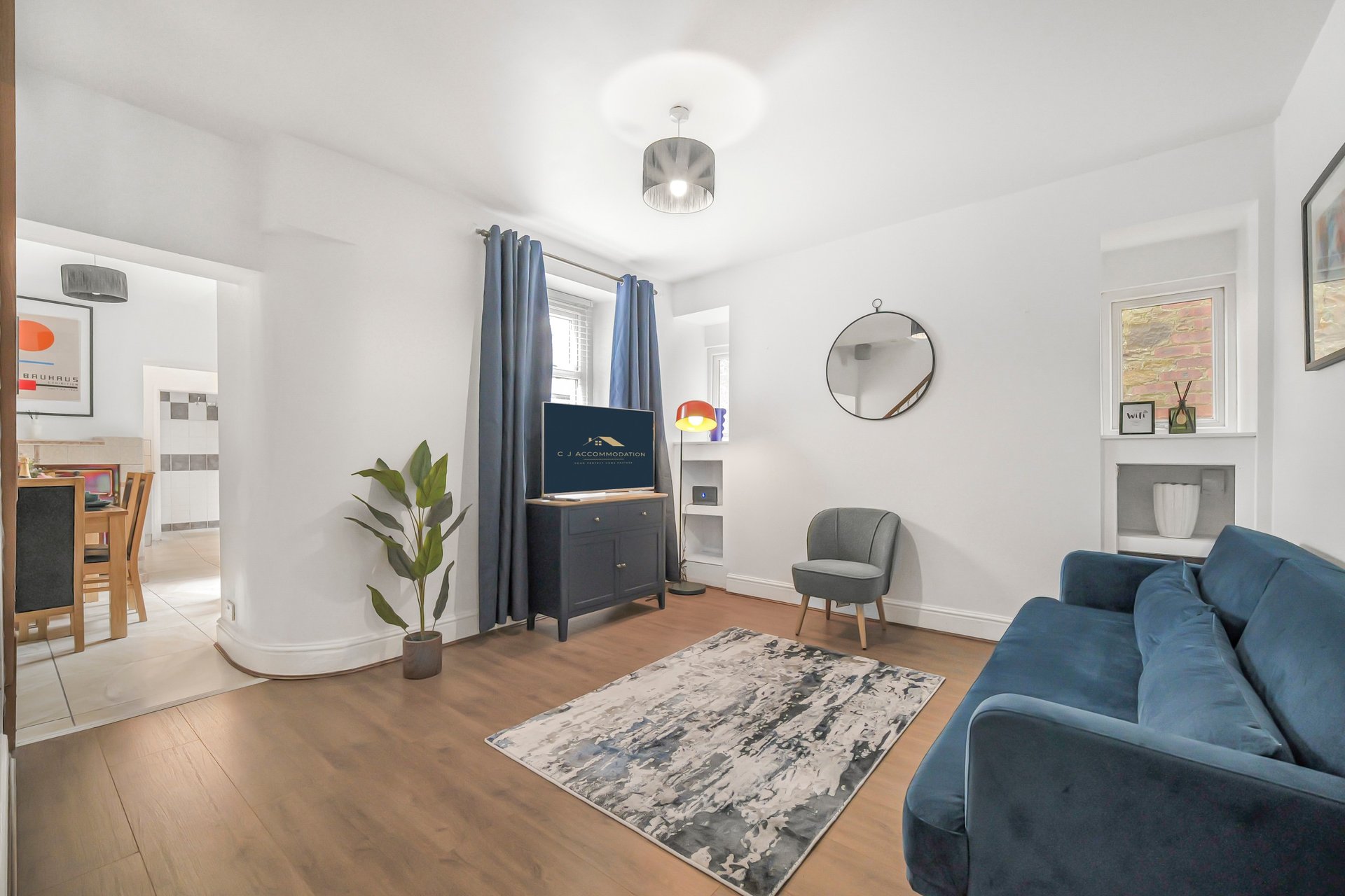 Bright living room with blue sofa, wooden floor, rug, potted plant and round wall clock
