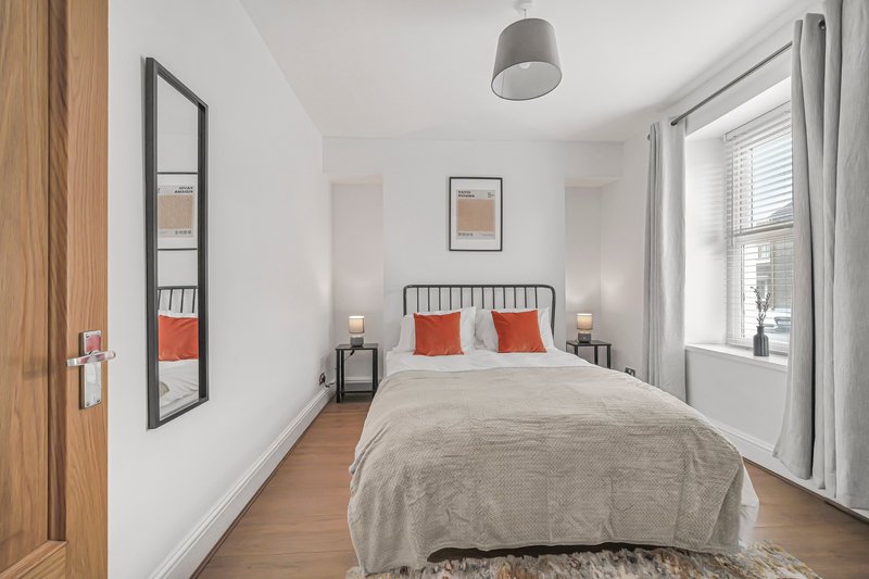 Bright bedroom with double bed, red pillows, wooden flooring and large window