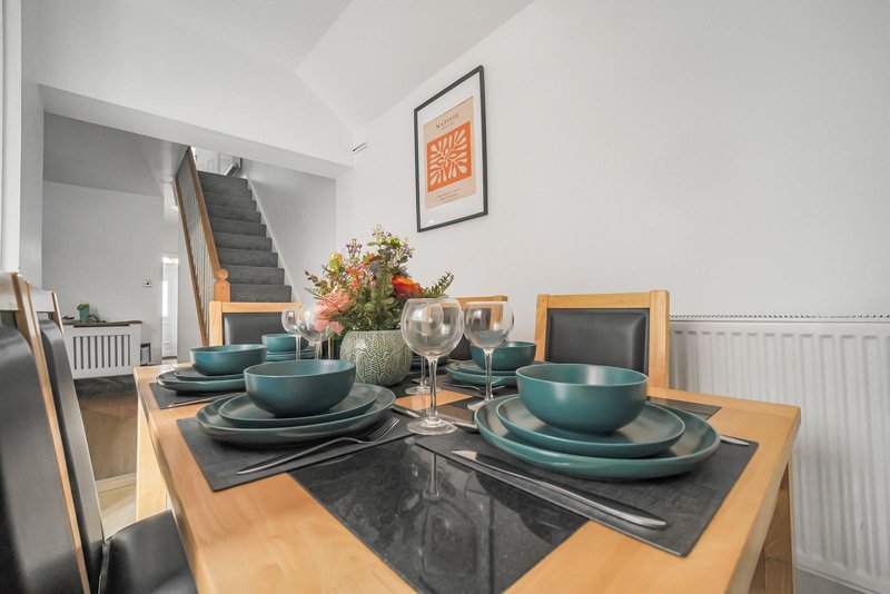 Dining table set with teal tableware, flowers, and glassware, open-plan kitchen visible behind