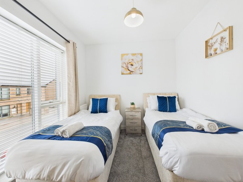 Twin bedroom with two single beds, blue bedding, wooden side table, and window with blinds