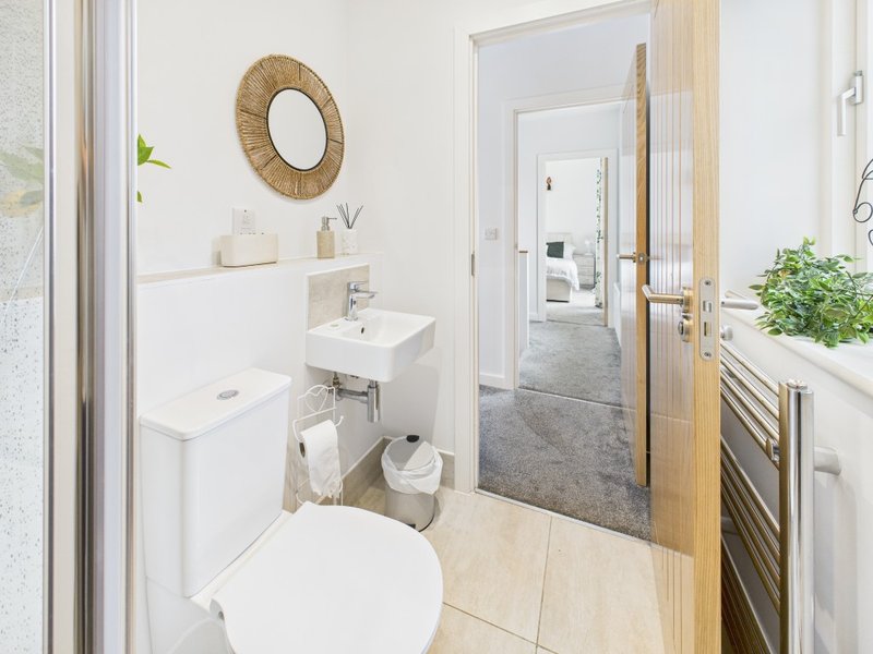 Modern bathroom with white toilet, sink, woven mirror and wooden door to hallway