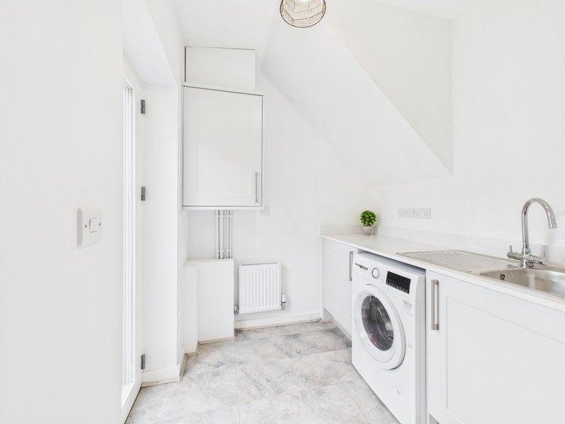 Modern utility room with washing machine, sink, white cabinetry and tiled floor