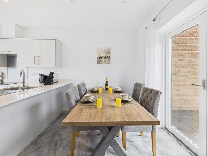 Modern kitchen-diner with white cabinetry, wooden dining table, grey chairs and yellow flowers