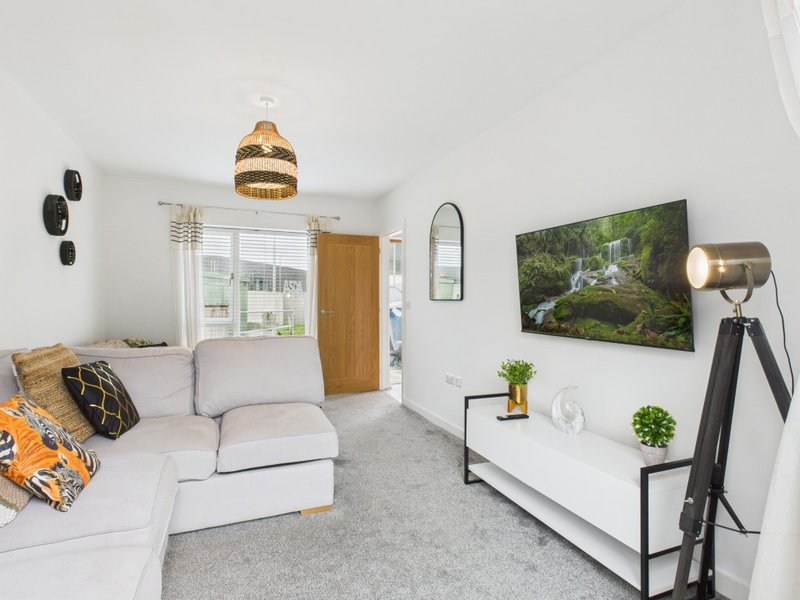 Bright living room with cream sectional sofa, wall-mounted TV, pendant lighting and decorative cushions