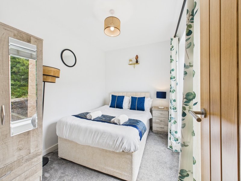 Bright bedroom with double bed, blue cushions, wooden pendant light and potted plants