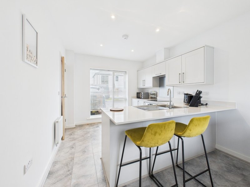 Modern white kitchen with island, yellow bar stools, and integrated appliances