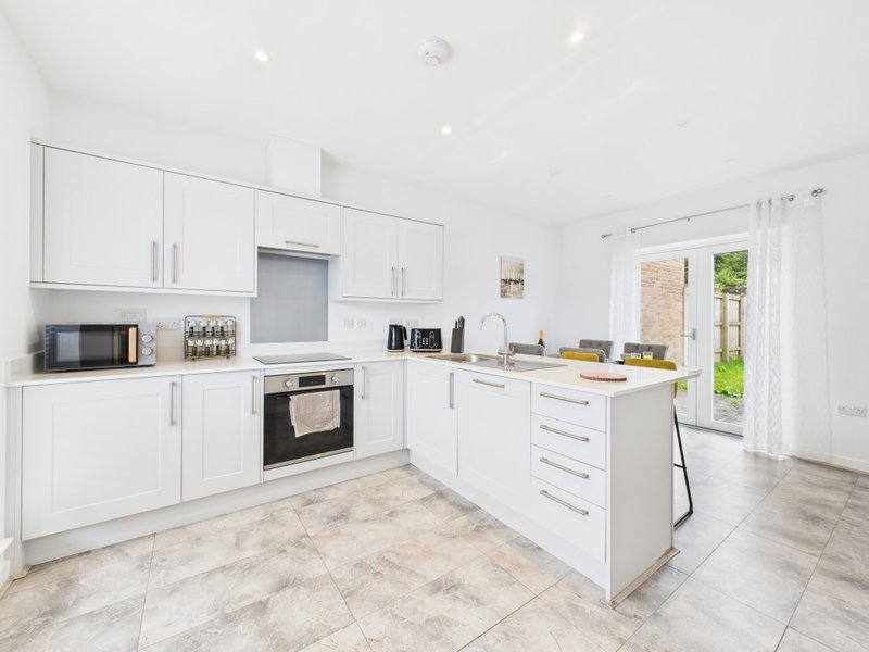 Modern white kitchen with island, built-in oven, and French doors to garden