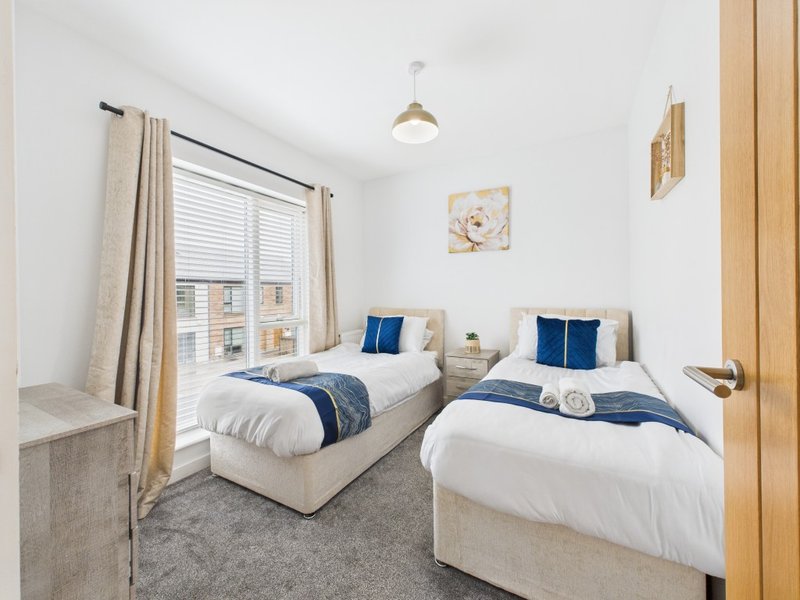 Twin bedroom with two single beds, blue cushions, wooden door and window with blinds
