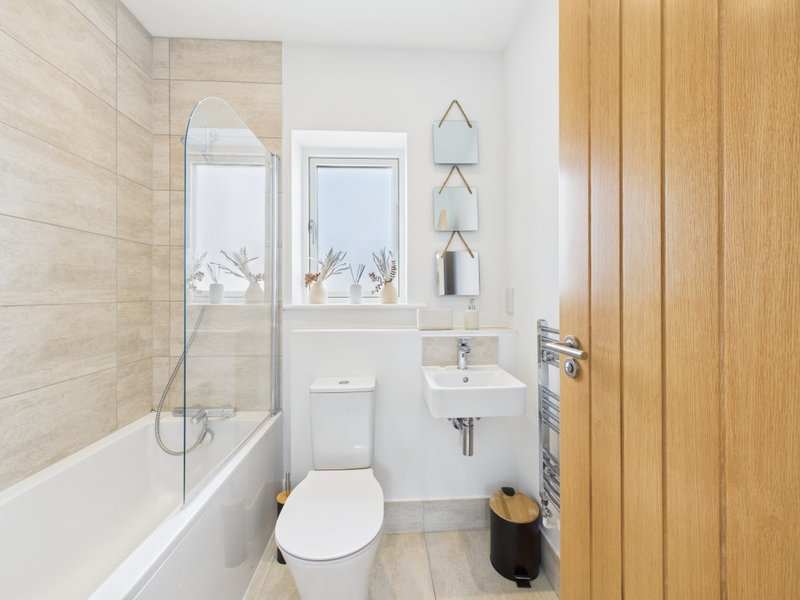 Modern bathroom with toilet, sink, bathtub, glass shower screen and wooden door