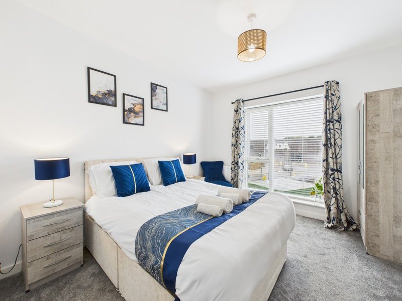Bright bedroom with double bed, blue cushions, wooden nightstands, and large window with view