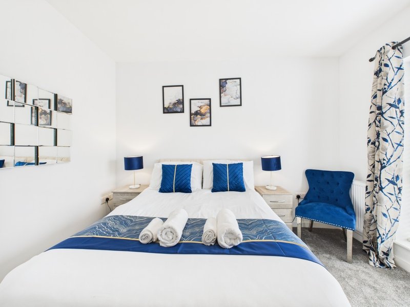 Modern bedroom with double bed, blue cushions, white bedding, and blue armchair